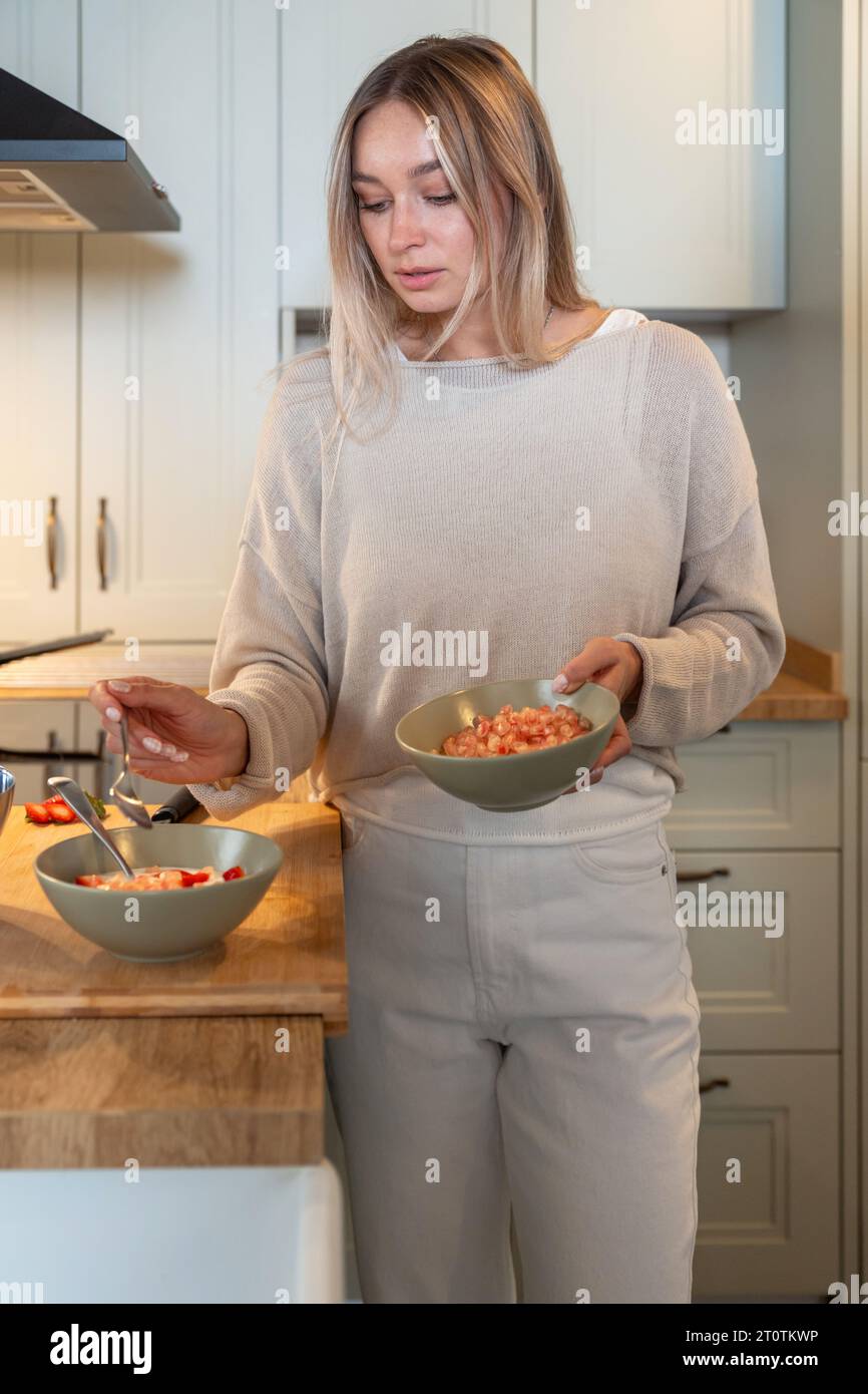 Donna caucasica che prepara un sano pasto a colazione con yogurt semplice, fragole e melograno sul bancone della cucina Foto Stock