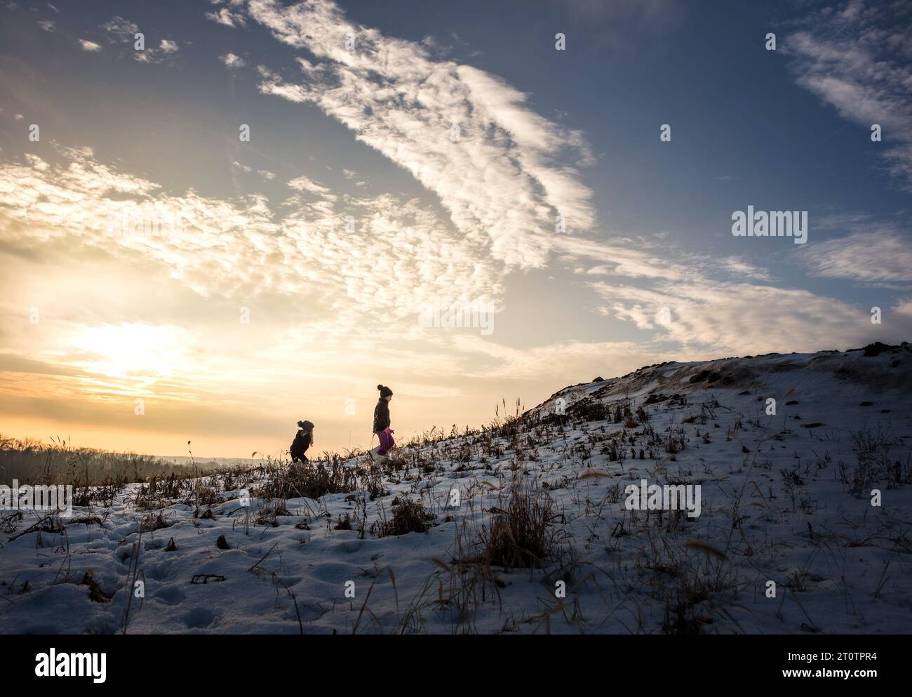 Sorelle che camminano su una collina innevata durante il tramonto Foto Stock