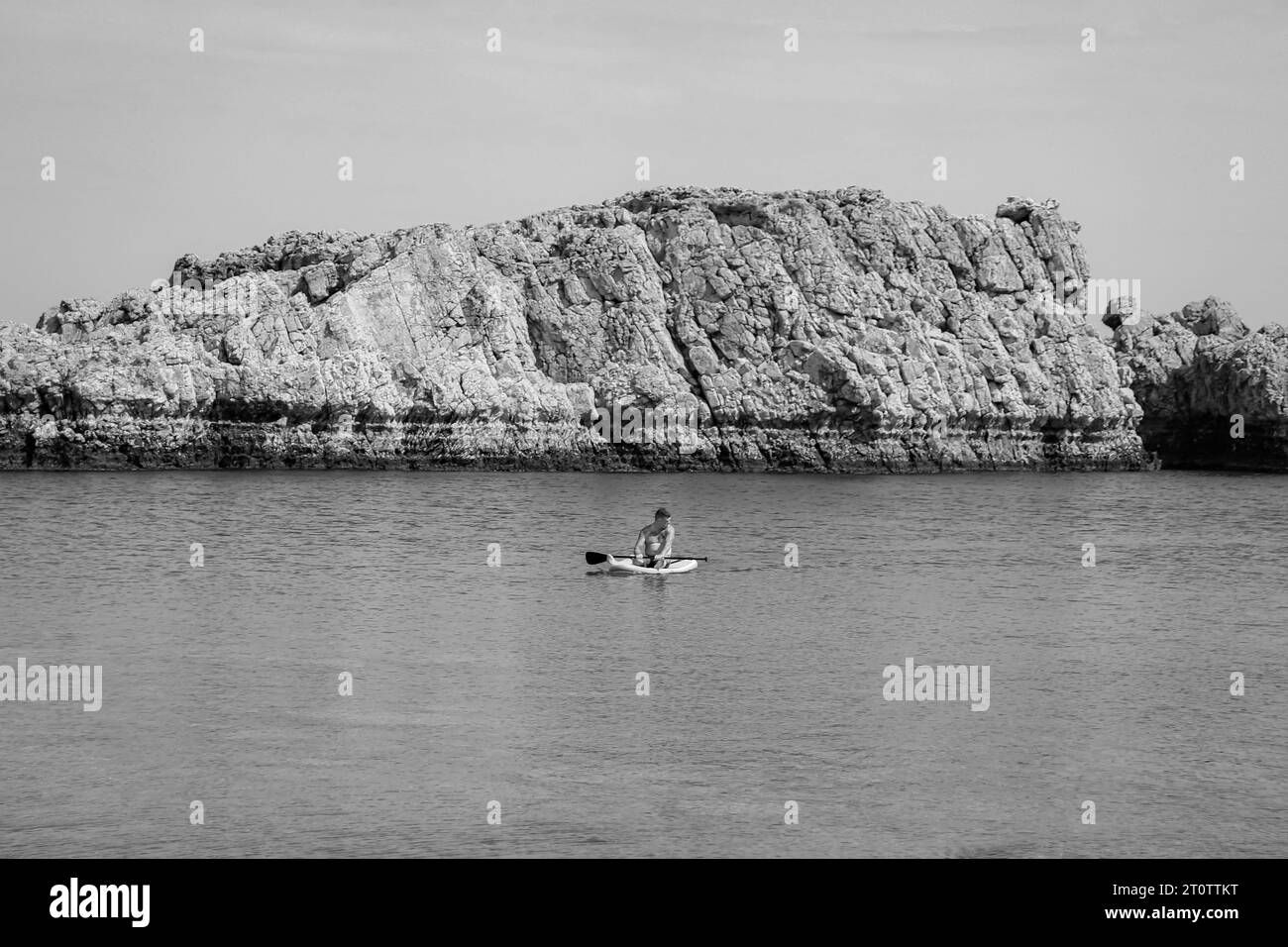 Uomo singolo seduto su una tavola da surf nell'acqua della spiaggia di Saint Paul's Bay in bianco e nero Foto Stock