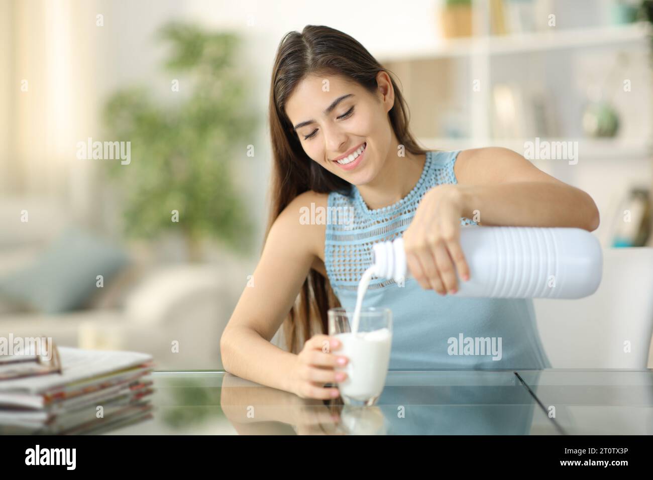 Donna felice che riempie il bicchiere con il latte seduta a casa Foto Stock