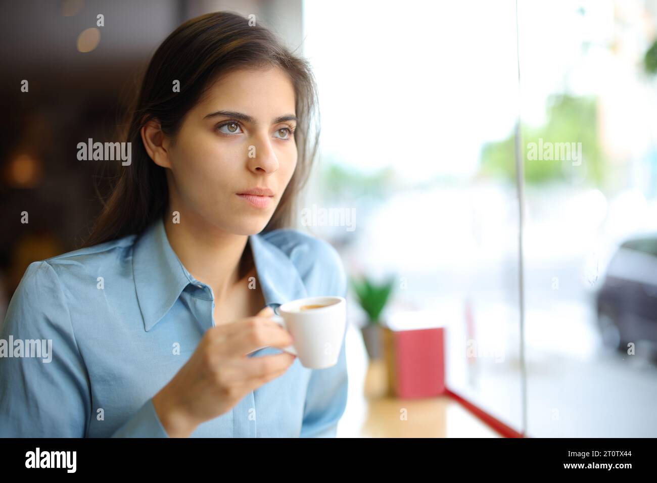 Donna distratta che beve caffè in un bar che guarda da una finestra Foto Stock