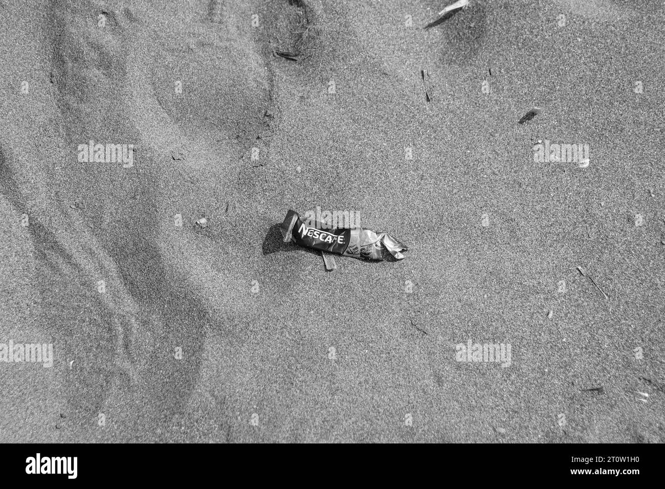 Pacchetto Nescafé a servizio singolo in bianco e nero lanciato sulla sabbia della spiaggia creando sporco, rifiuti e inquinamento vicino all'oceano in natura Foto Stock