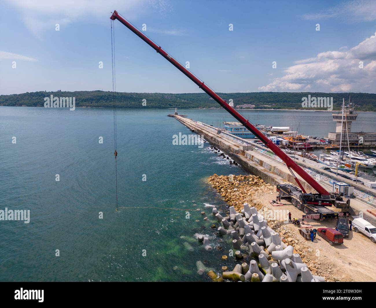 Vista aerea dall'alto della costruzione di frangiflutti. Bulldozer e gru su un mucchio di massi nel mare Foto Stock