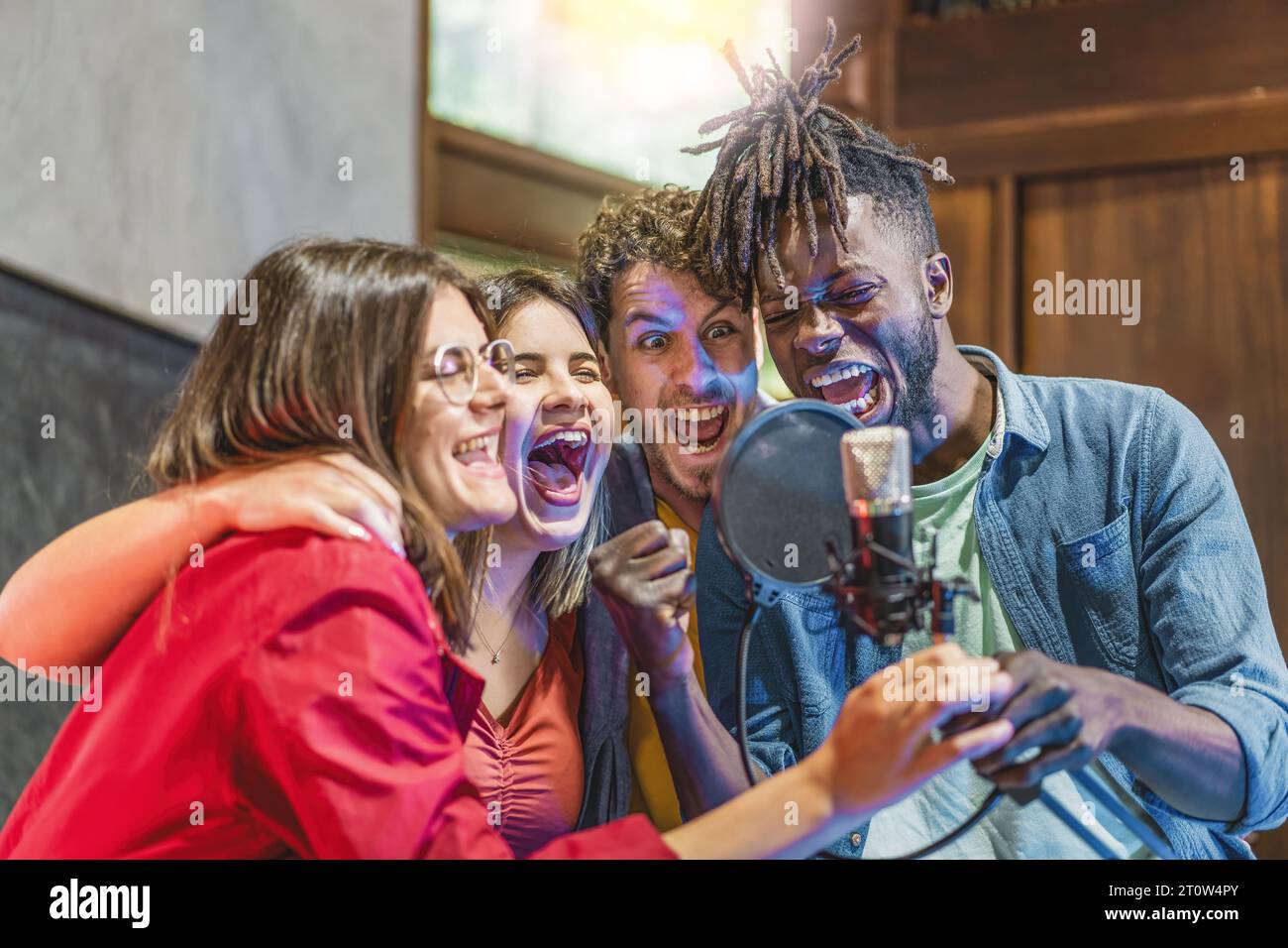 Un gruppo eterogeneo di giovani uomini e donne che canta con fervore intorno a un microfono a condensatore, mostrando il loro entusiasmo e la loro passione musicale. Foto Stock