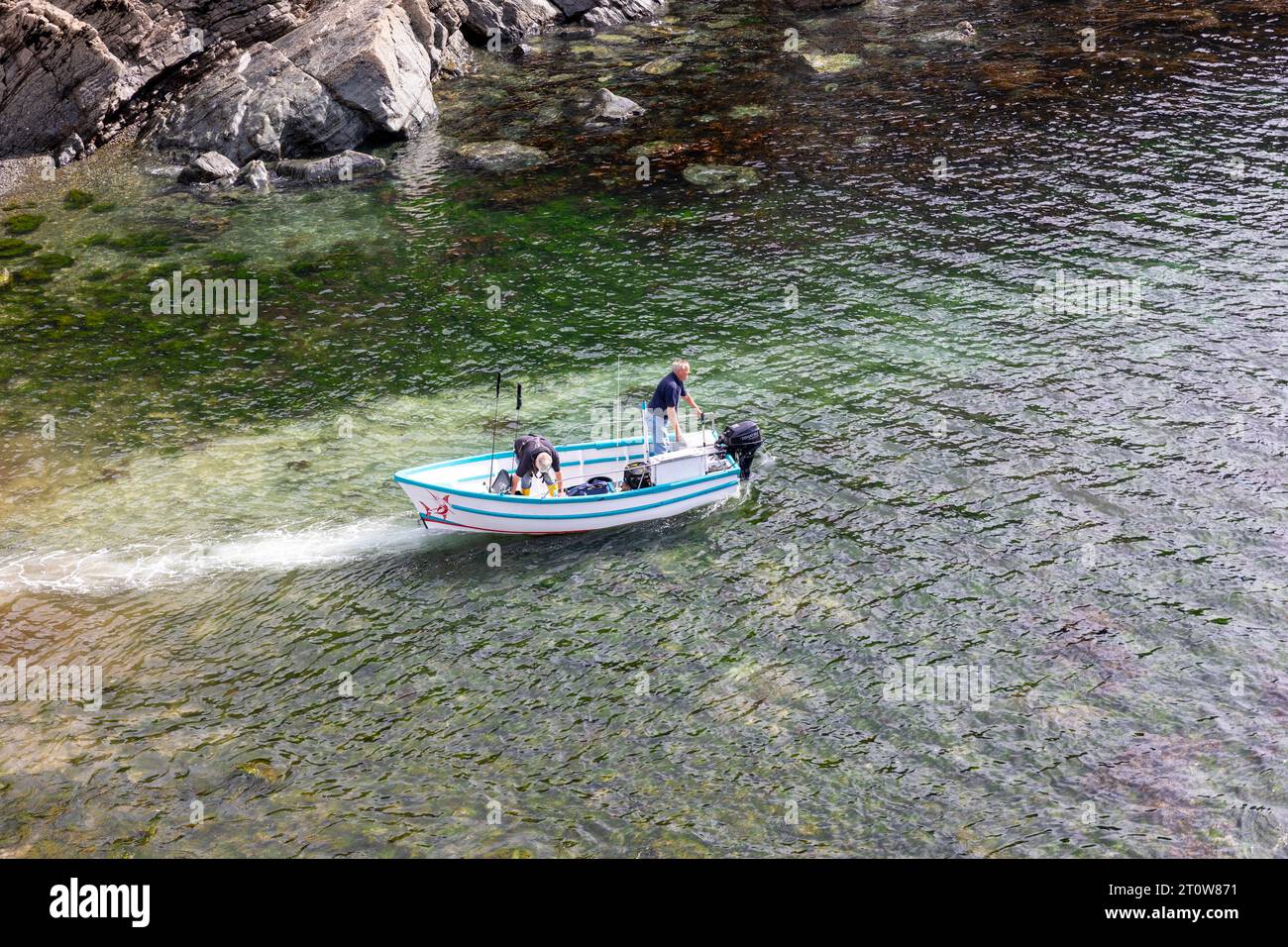 Cadgwith villaggio sulla penisola di Lizard, Cornovaglia, Inghilterra i pescatori in una piccola barca da pesca nelle strette acque lasciano la baia, UK,2023 Foto Stock