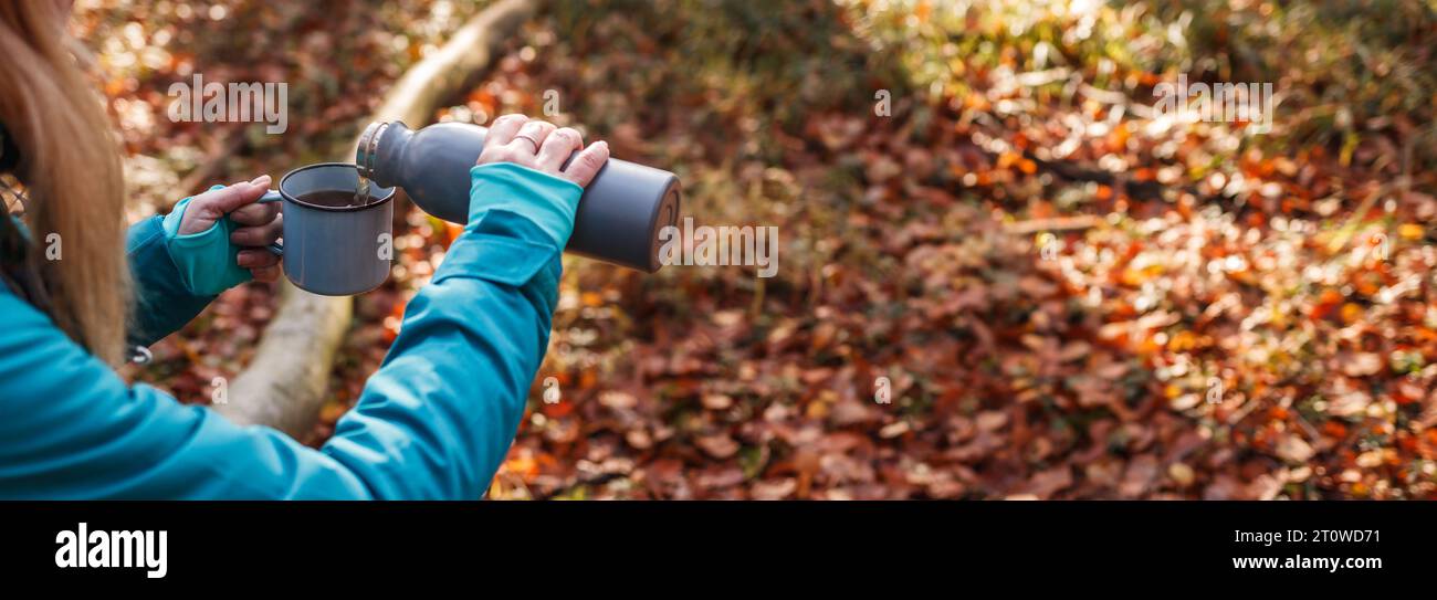 Escursionista che versa bevande calde dal thermos nella tazza da viaggio nella foresta autunnale. Ristoro durante le escursioni nella natura. Vista panoramica Foto Stock