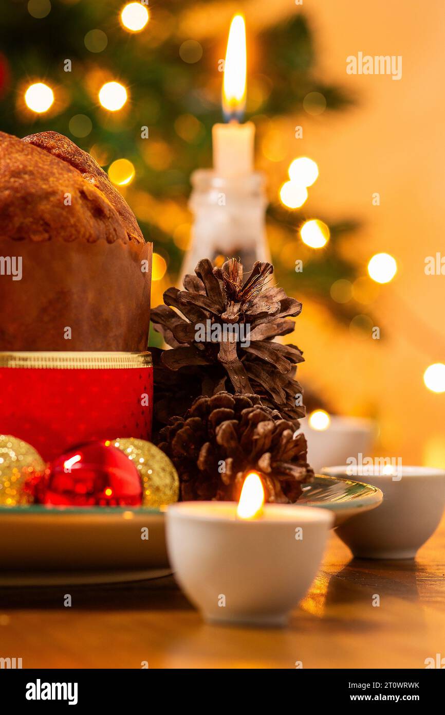 Goiânia, Goias, Brasile – 8 ottobre 2023: Panettone, coni di pino, candele accese, palle e albero di Natale sullo sfondo con luci bokeh. Foto Stock