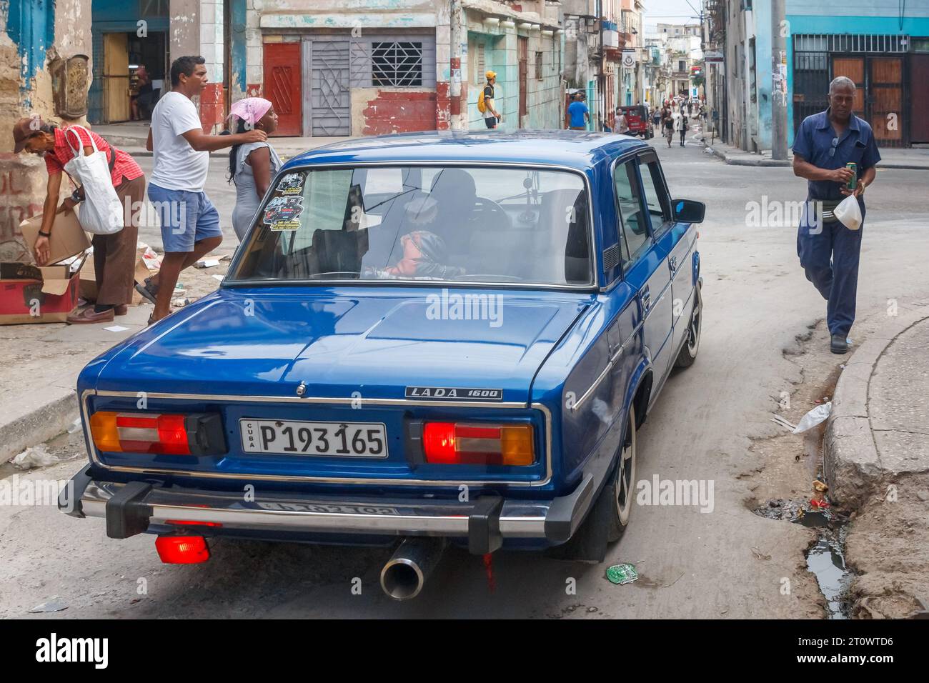 Un'auto Lada guidata in una strada cittadina da persone cubane che vivono nel loro normale stile di vita. Il marciapiede è rotto e sporco. Gli edifici sono intemprati a Foto Stock