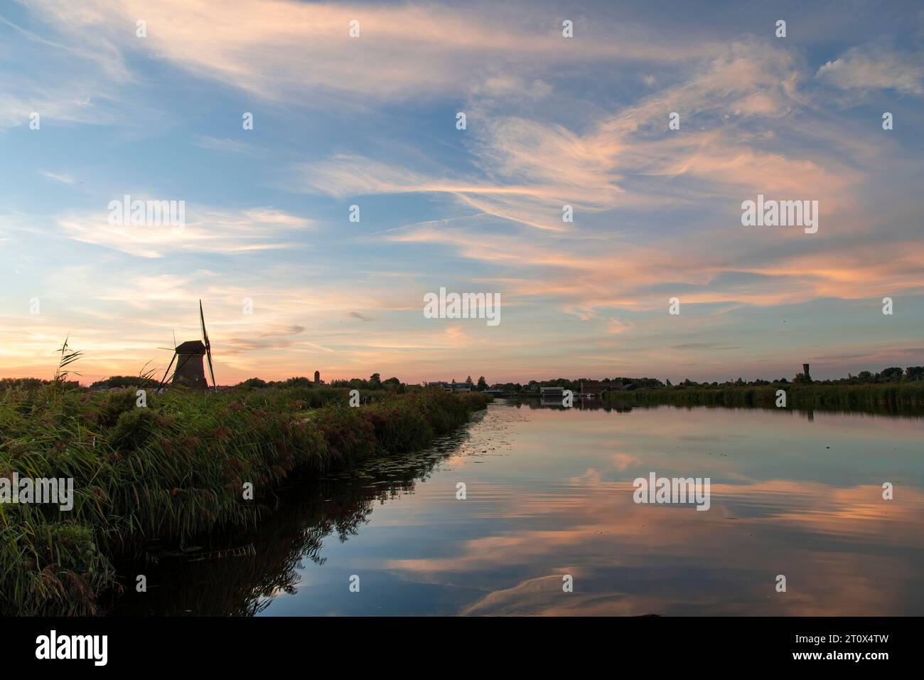 Vista del tramonto su acque tranquille con letti di canne di un canale con riflesso perfetto delle nuvole del tramonto sull'acqua accanto alla silhouette dell'iconico XVIII secolo Foto Stock