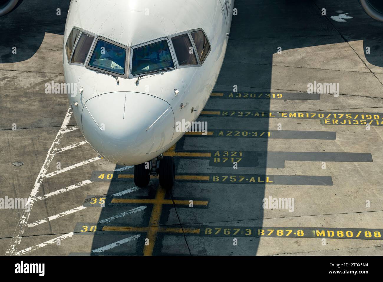Vista ravvicinata ad angolo elevato della cabina di pilotaggio di un aeromobile parcheggiato su contrassegni gialli dell'aeroporto sull'asfalto di fronte al cancello Foto Stock