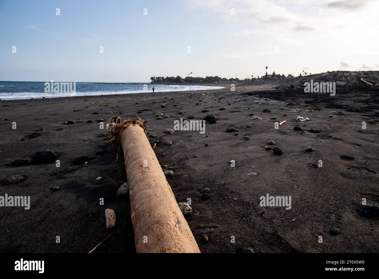 Ein schwarzer Sandstrand direkt am Meer. Schoene Landschaft mit Wellen am Abend auf dem Meer auf der tropischen Insel a Sanur, Bali, Indonesia Foto Stock