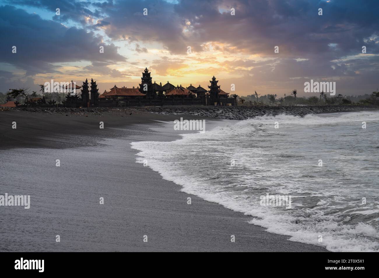 Tempio indù su una spiaggia di sabbia nera direttamente sul mare. Paesaggio serale con onde sul mare sull'isola tropicale di Sanur, Bali, Indonesia Foto Stock