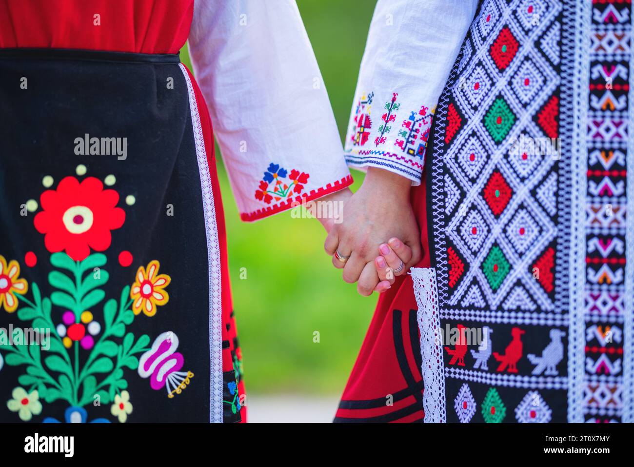 Ragazze in costumi etnici bulgari tradizionali con ricami folcloristici che si tengono per mano. Lo spirito di casa Bulgaria - cultura, storia e tradizioni. Foto Stock