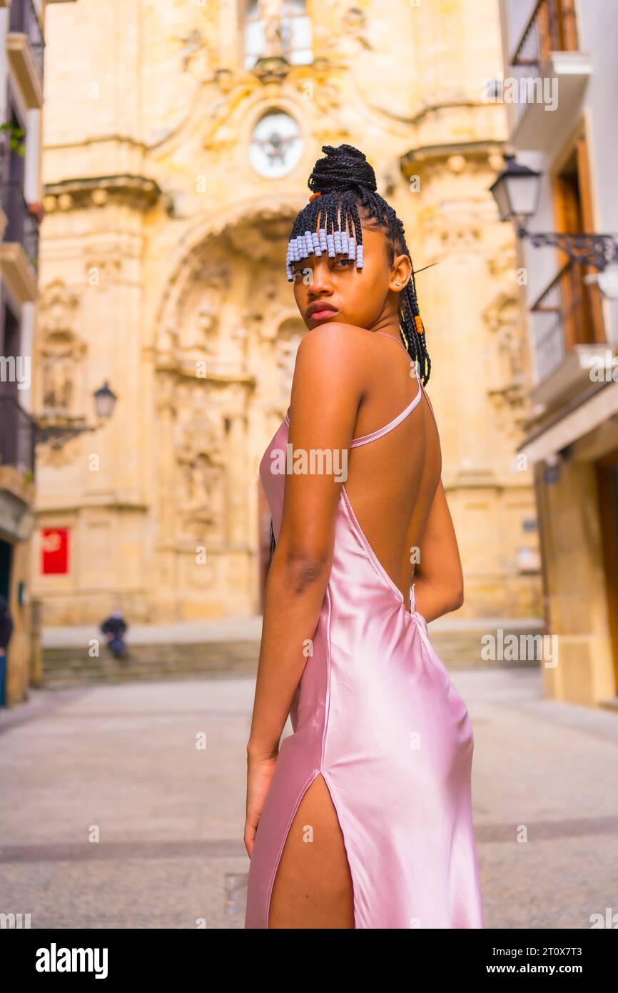 Ragazza etnica dominicana con trecce e un bellissimo vestito rosa. La moda si gode l'estate in una bella chiesa della città Foto Stock