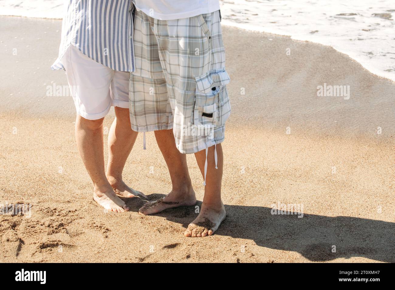 Le gambe di una coppia sposata anziana si trovano sulla spiaggia vicino al mare. Foto Stock