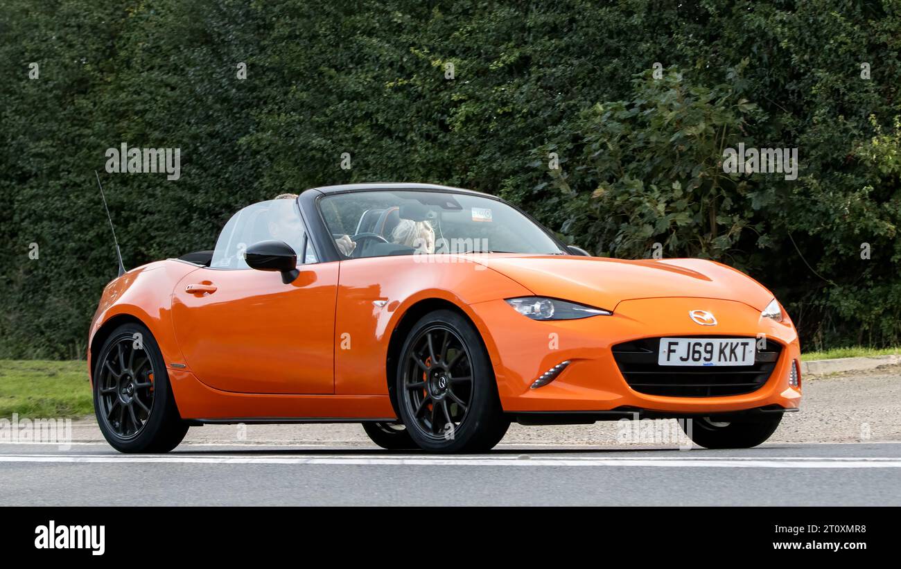 Bicester, Oxon., UK - 8 ottobre 2023: 2019 auto d'epoca Mazda MX5 arancione che guida su una strada di campagna inglese. Foto Stock