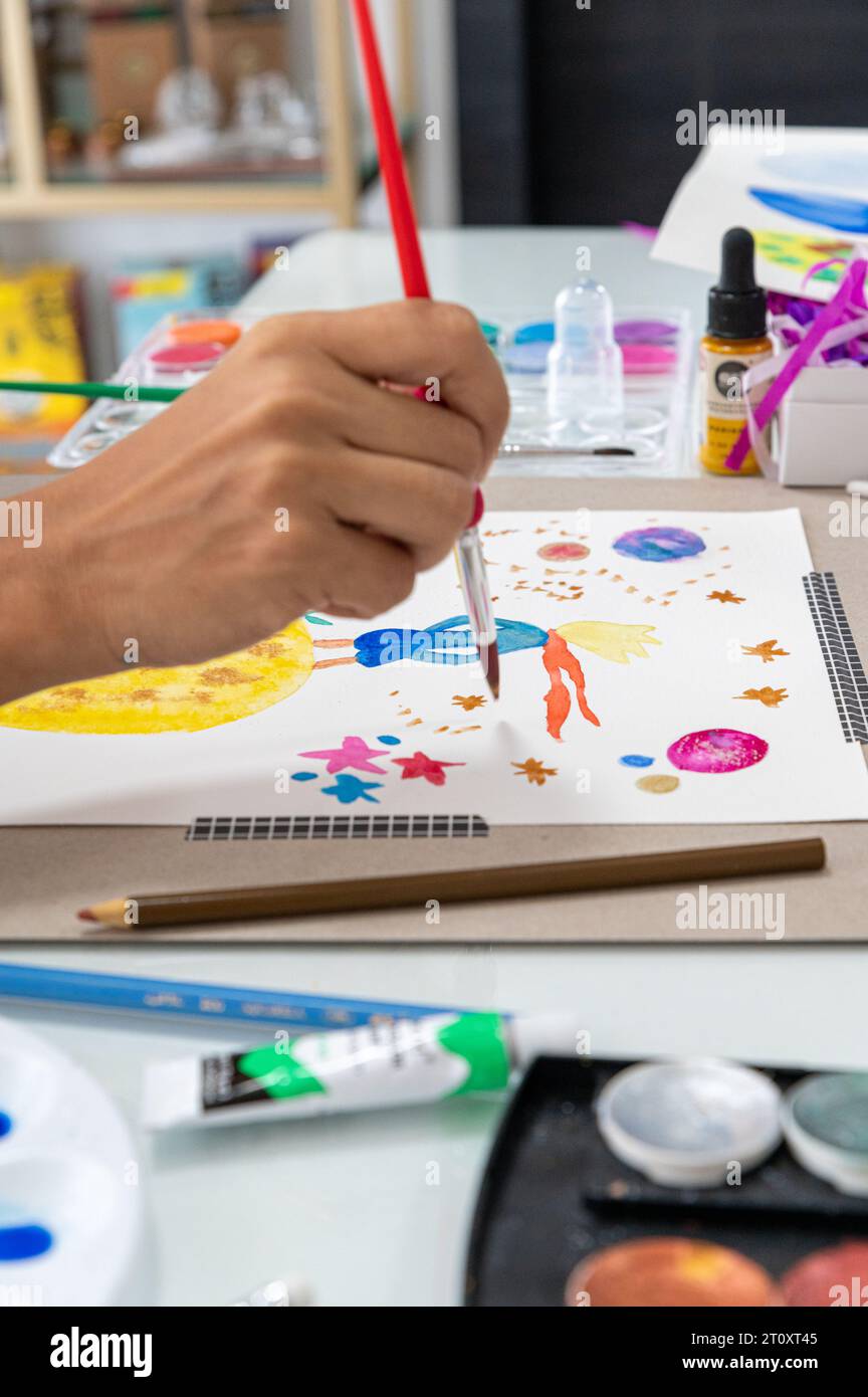 Primo piano della mano che tiene una spazzola e dipinge con acquerello su un tavolo. Anche un bel design astratto colorato. Molto colorato Foto Stock