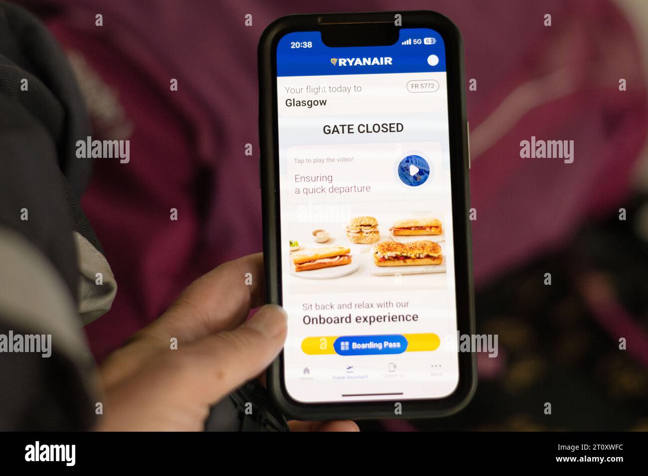 Volo perso - passeggero che guarda il messaggio di chiusura del cancello sull'app del telefono Ryanair con le borse sul tram dell'aeroporto sullo sfondo Foto Stock