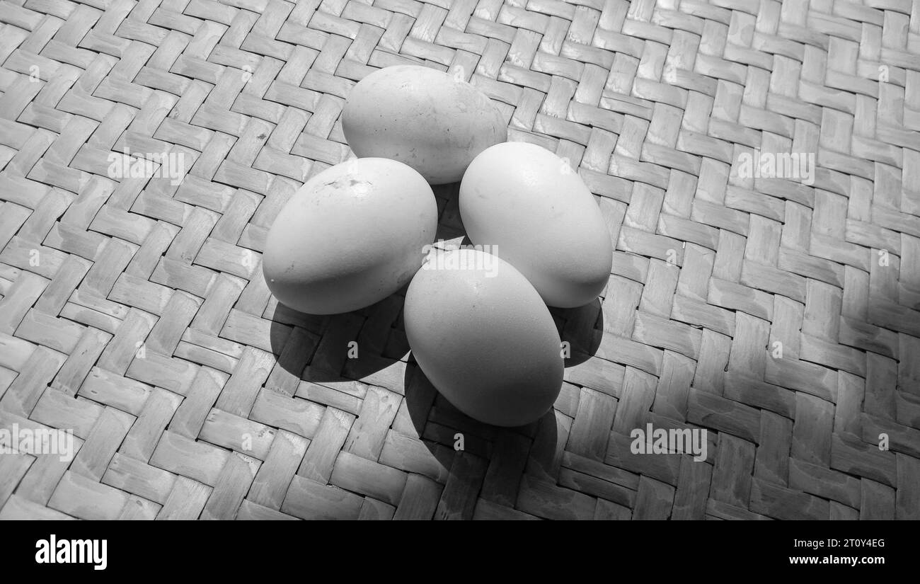 Foto di 4 uova di gallina su un tema bianco e nero su uno sfondo di bambù intrecciato Foto Stock