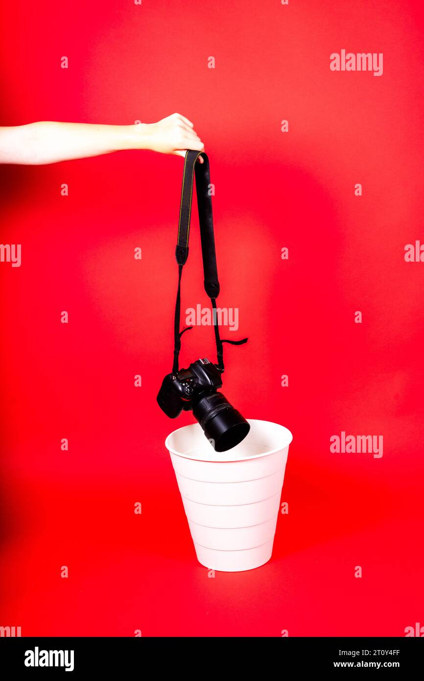 Mano con la vecchia fotocamera digitale in un cestino, isolato su sfondo rosso Foto Stock