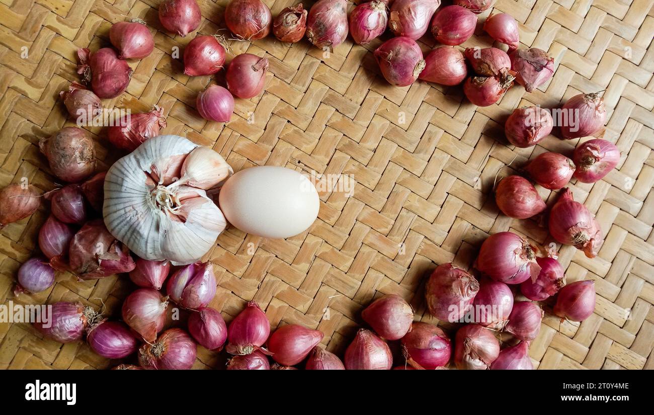 Foto di spezie sotto forma di scalogni, aglio, peperoncini e uova disposte in un bambù intrecciato Foto Stock