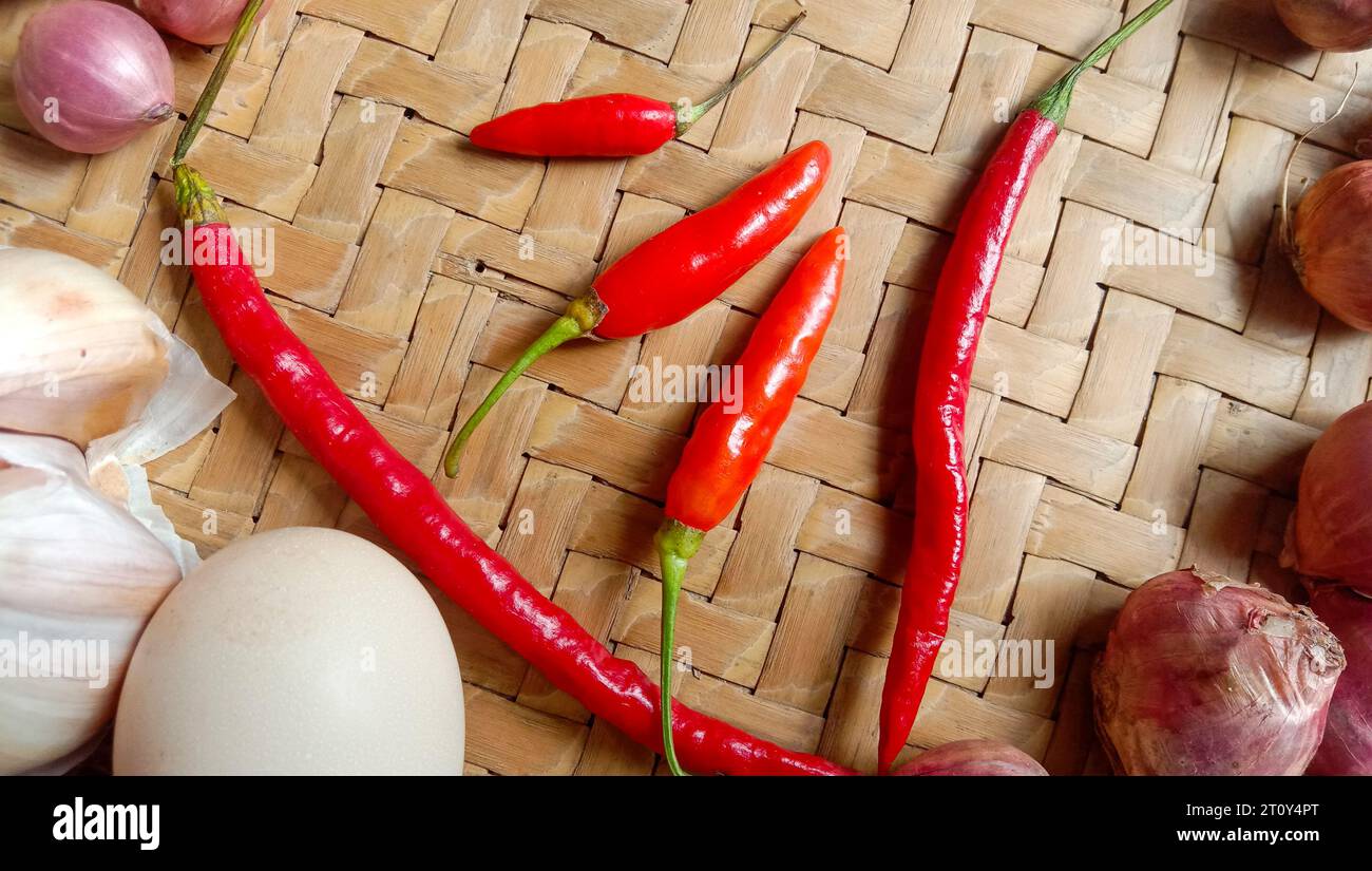 Foto di spezie sotto forma di scalogni, aglio, peperoncini e uova disposte in un bambù intrecciato Foto Stock