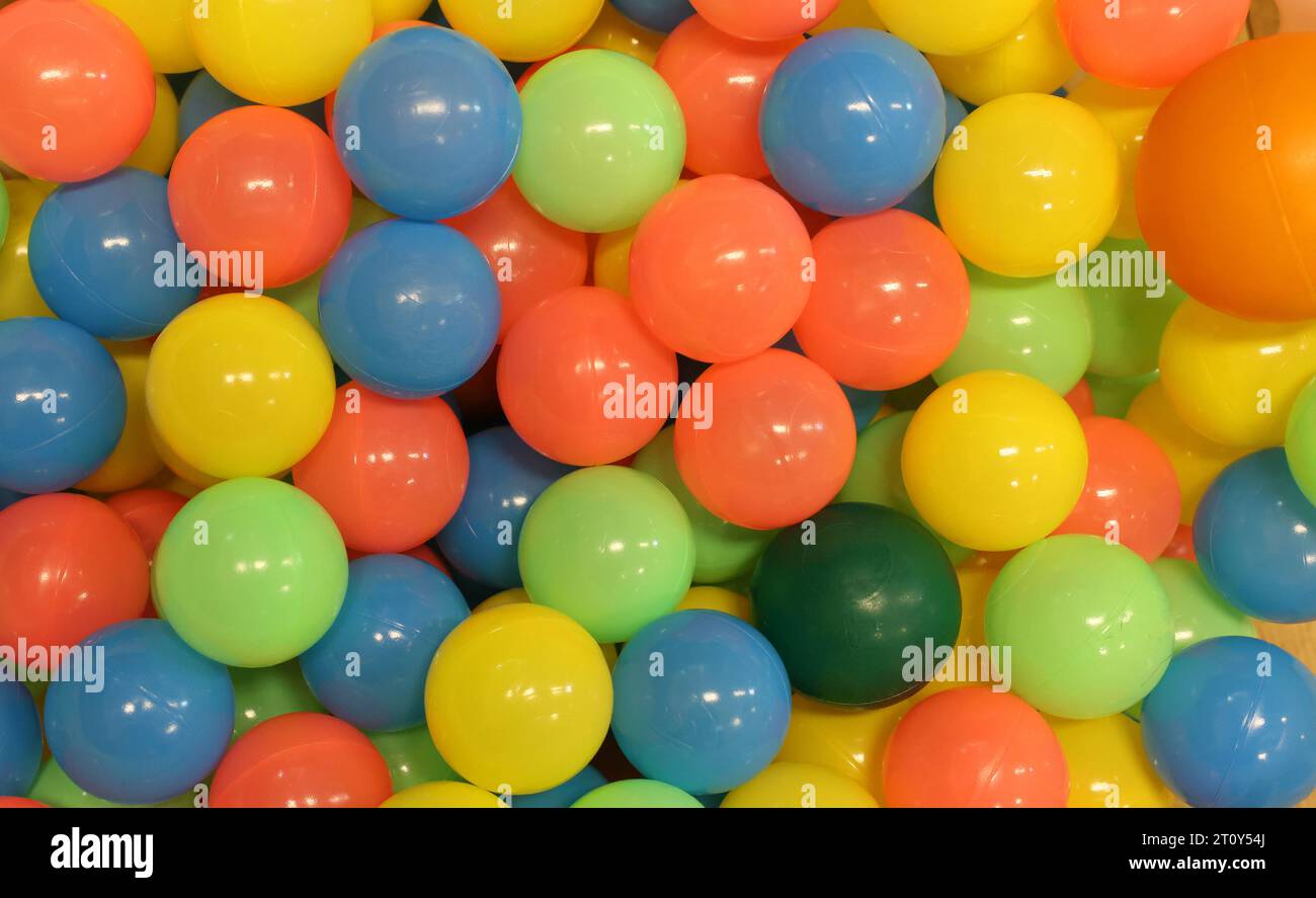 Una collezione di palline di plastica dai colori vivaci che si trovano in un campo da baseball per bambini o in un centro di attività per il divertimento. Palline colorate rotonde circolari in un campo da gioco. Divertimento per i bambini Foto Stock
