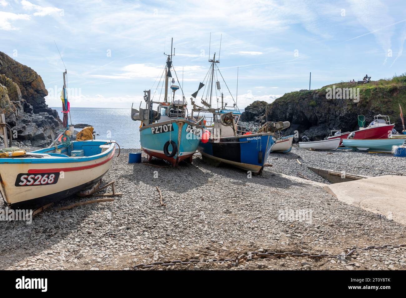 Cadgwith villaggio sulla penisola di Lizard, Cornovaglia, Inghilterra, con barche da pesca sulla spiaggia del porto e vista del promontorio della baia Foto Stock