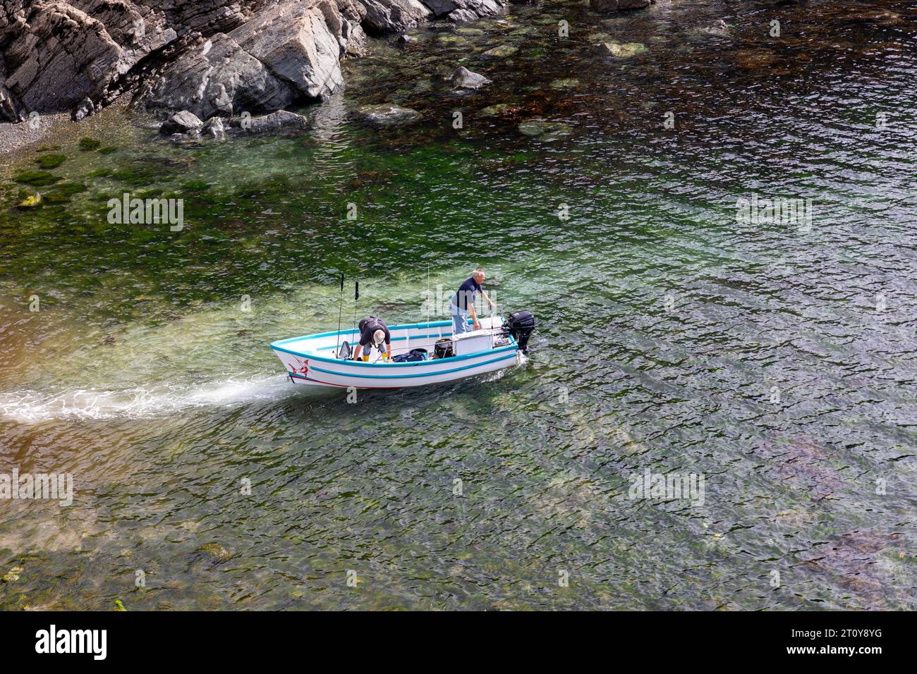 Cadgwith, villaggio sulla penisola di Lizard, Cornovaglia, pescatori inglesi in una piccola barca da pesca, lasciano l'insenatura Foto Stock