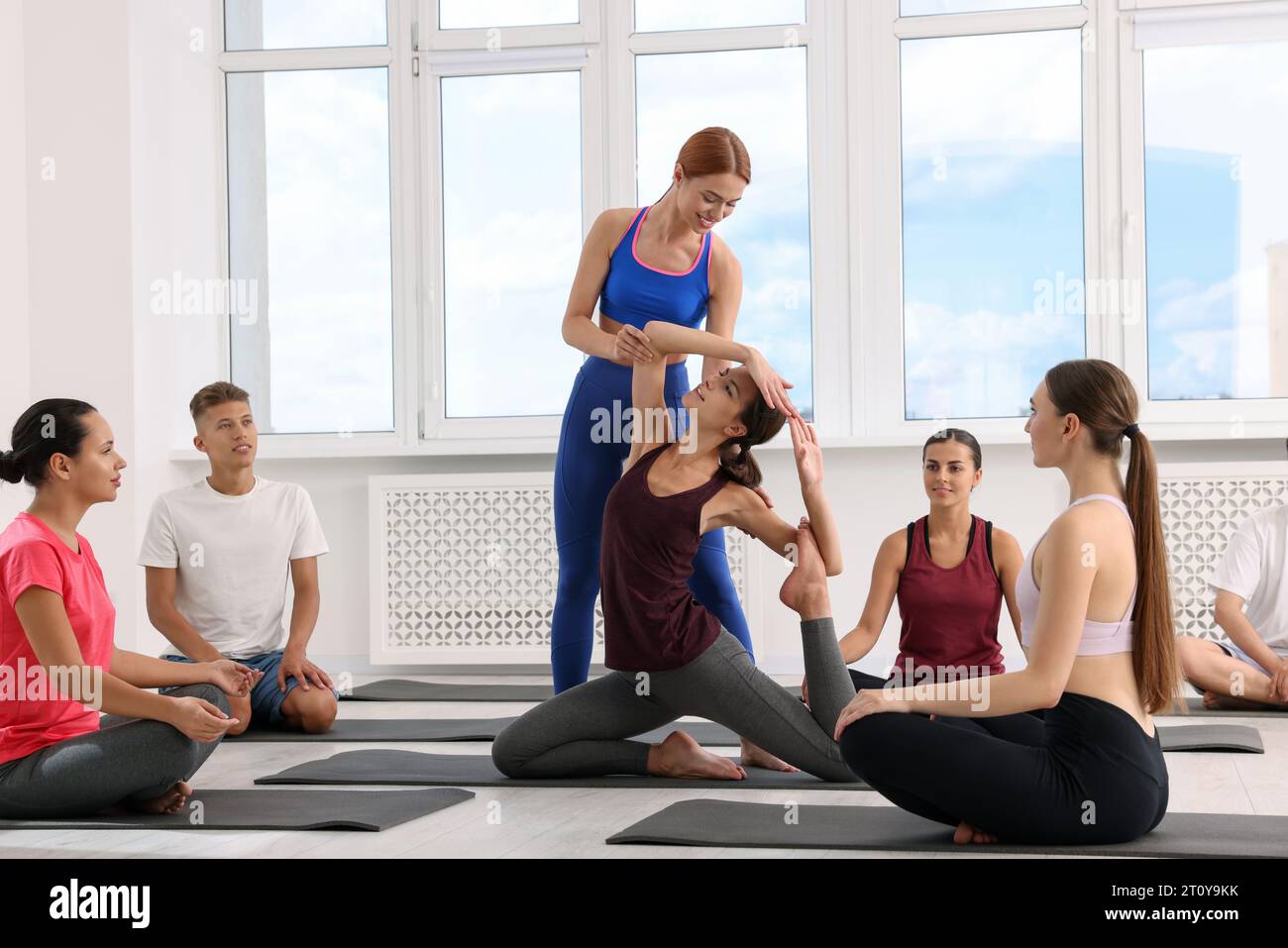 Allenatore di yoga che aiuta le donne durante le lezioni di gruppo al chiuso Foto Stock
