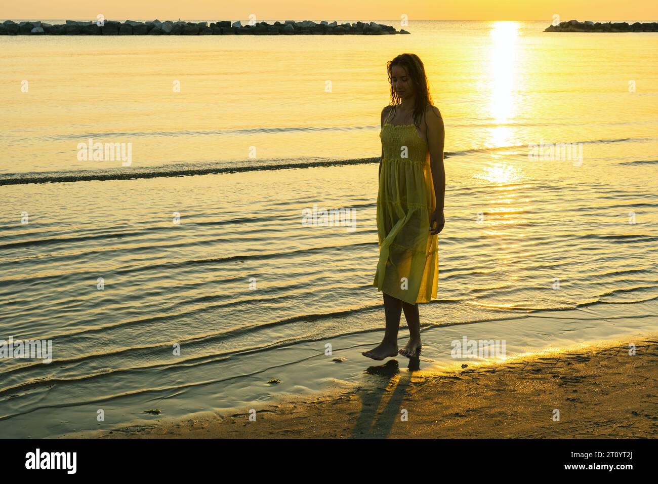 Una giovane donna cammina lungo la spiaggia all'alba e condivide il suo viaggio avventuroso. Foto Stock