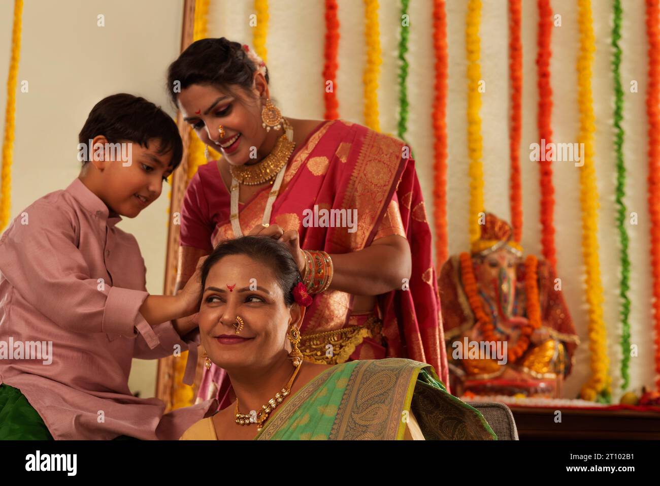 Ragazzo che aiuta sua madre a legare i capelli di sua nonna durante Ganesh Chaturthi, una festa celebrata nel Maharashtra (India occidentale) Foto Stock