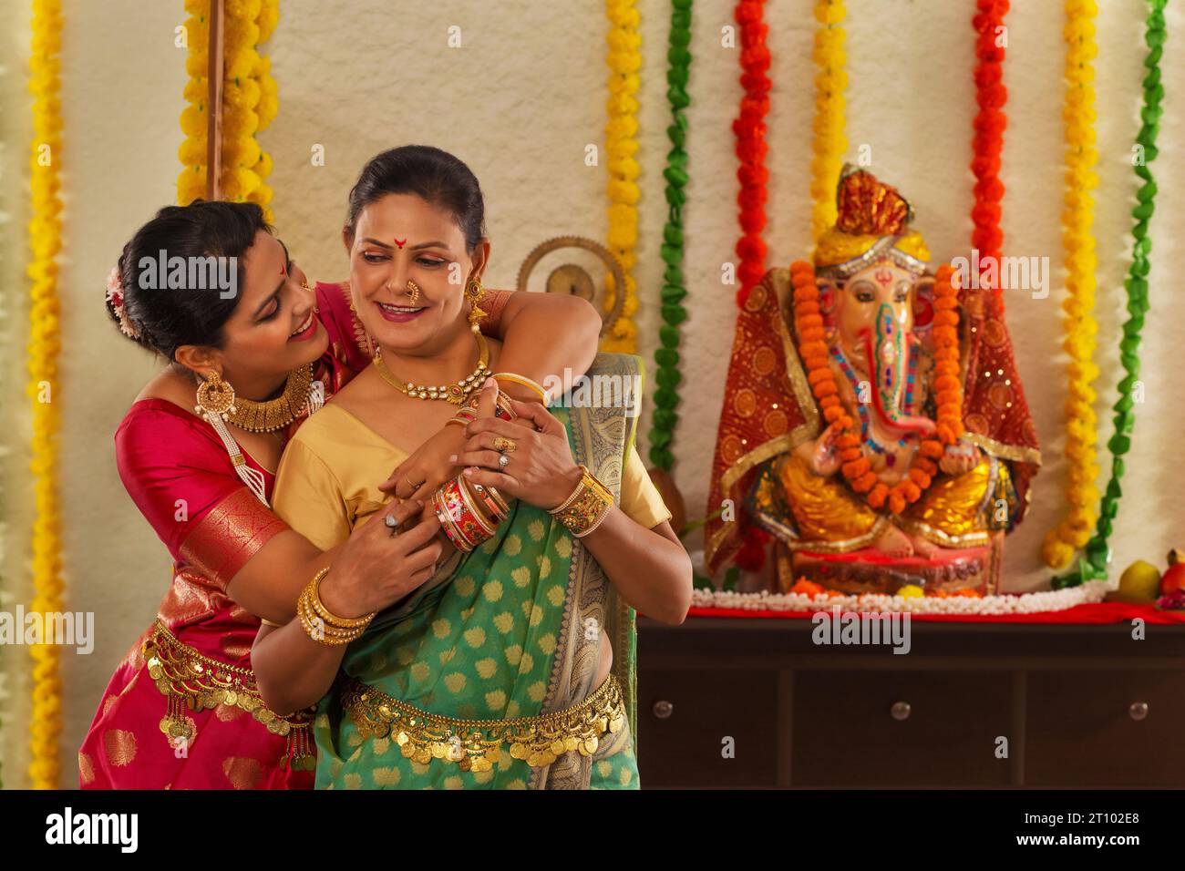 Nuora che abbraccia sua suocera di fronte all'idolo Ganesh Foto Stock
