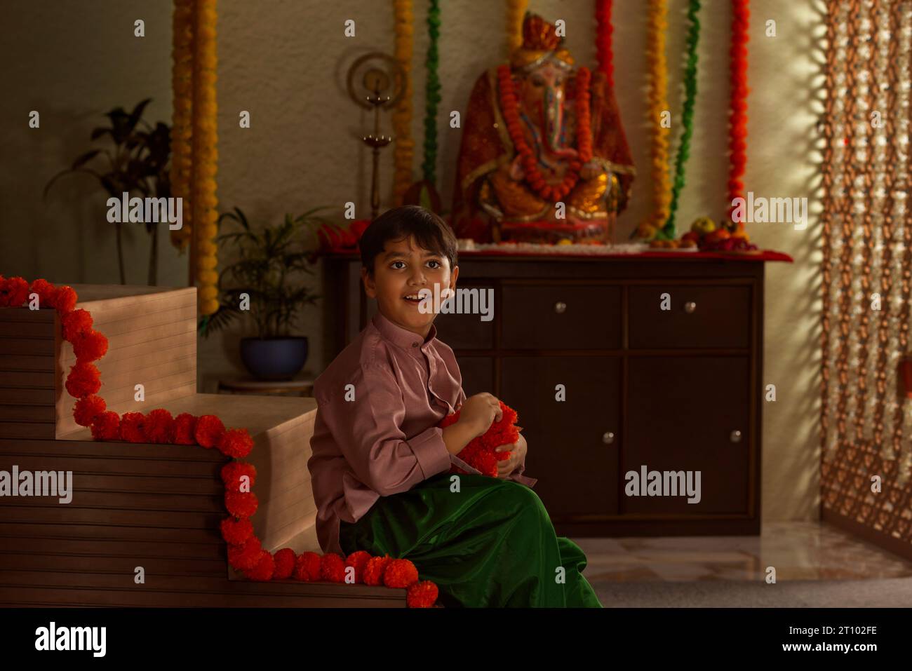 Bambino che decora casa con ghirlande di fiori a Ganesh Chaturthi Foto Stock