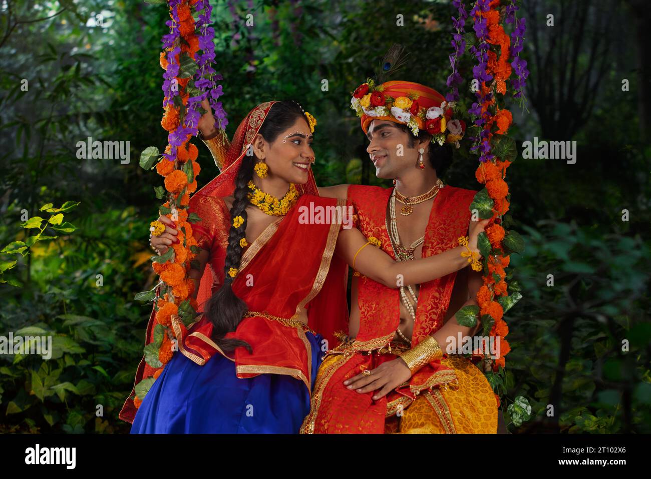 Giovane uomo e donna vestiti da Radha e Krishna e seduti insieme su un altalena in occasione di Janmashtami Foto Stock