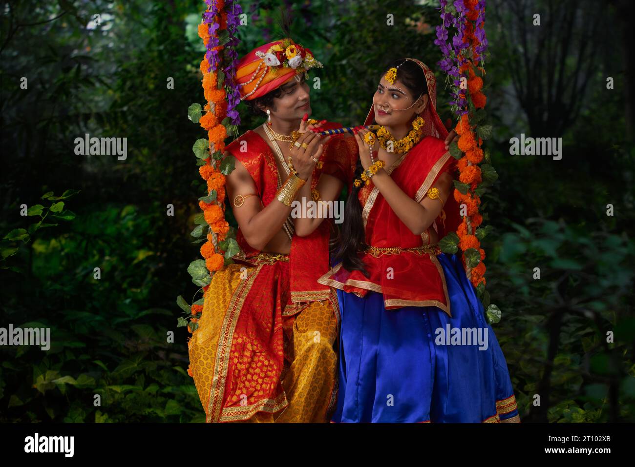 Giovane uomo e donna vestiti da Radha e Krishna e seduti insieme su un altalena in occasione di Janmashtami Foto Stock