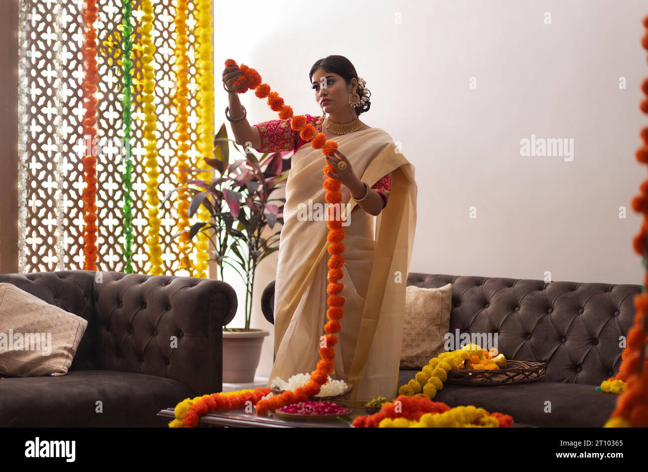 Donna in sari bianchi che decora casa con ghirlande di fiori per celebrare l'Onam Foto Stock