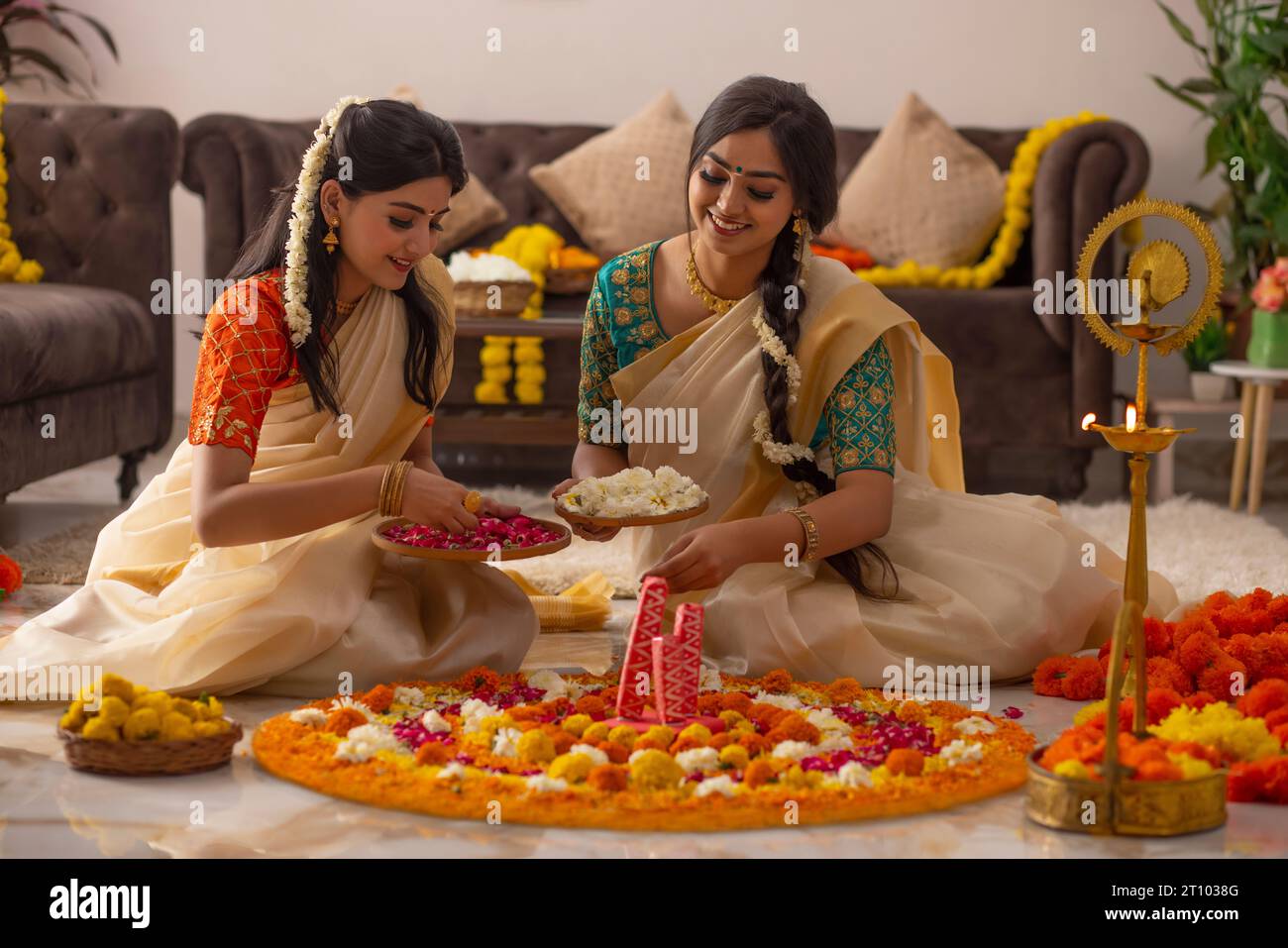 Donne dell'India meridionale in sari bianchi che decorano il pavimento con fiori per celebrare l'onam Foto Stock
