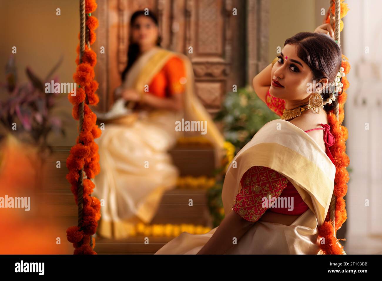 Donne in sari bianchi sedute su un altalena su Onam Foto Stock