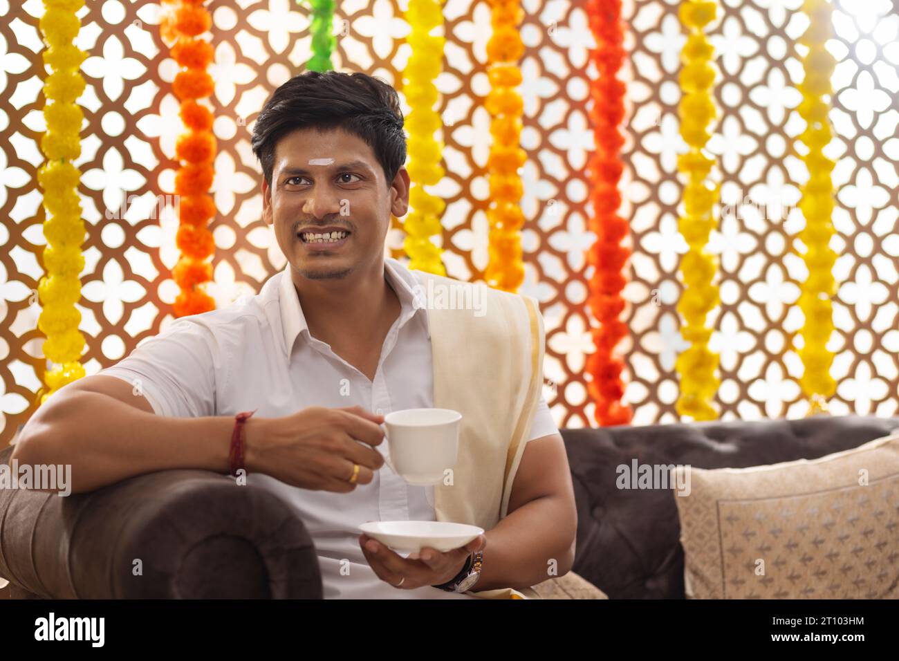 Un uomo dell'India meridionale che beve tè mentre sedeva sul divano nel soggiorno Foto Stock