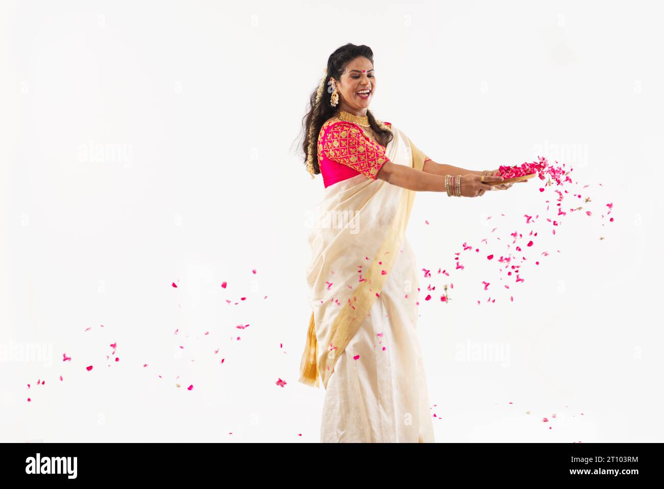 Donna sorridente in abiti tradizionali che soffiano petali di rosa sullo sfondo del dolore Foto Stock