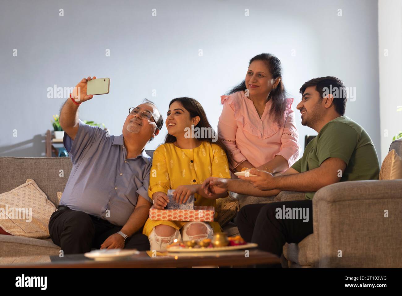 Uomo anziano che scatta selfie della sua famiglia mentre si siede insieme a casa a Raksha Bandhan Foto Stock