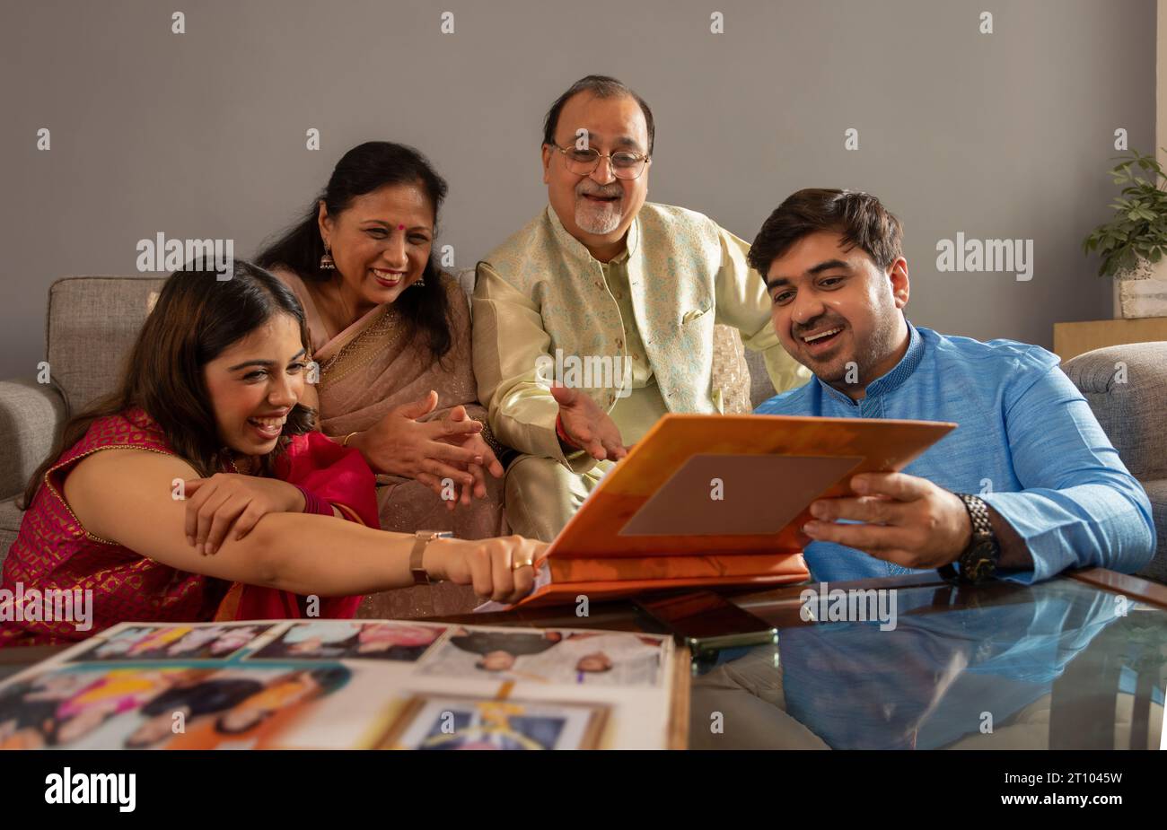 Una famiglia indiana felice che guarda un album fotografico insieme a casa Foto Stock