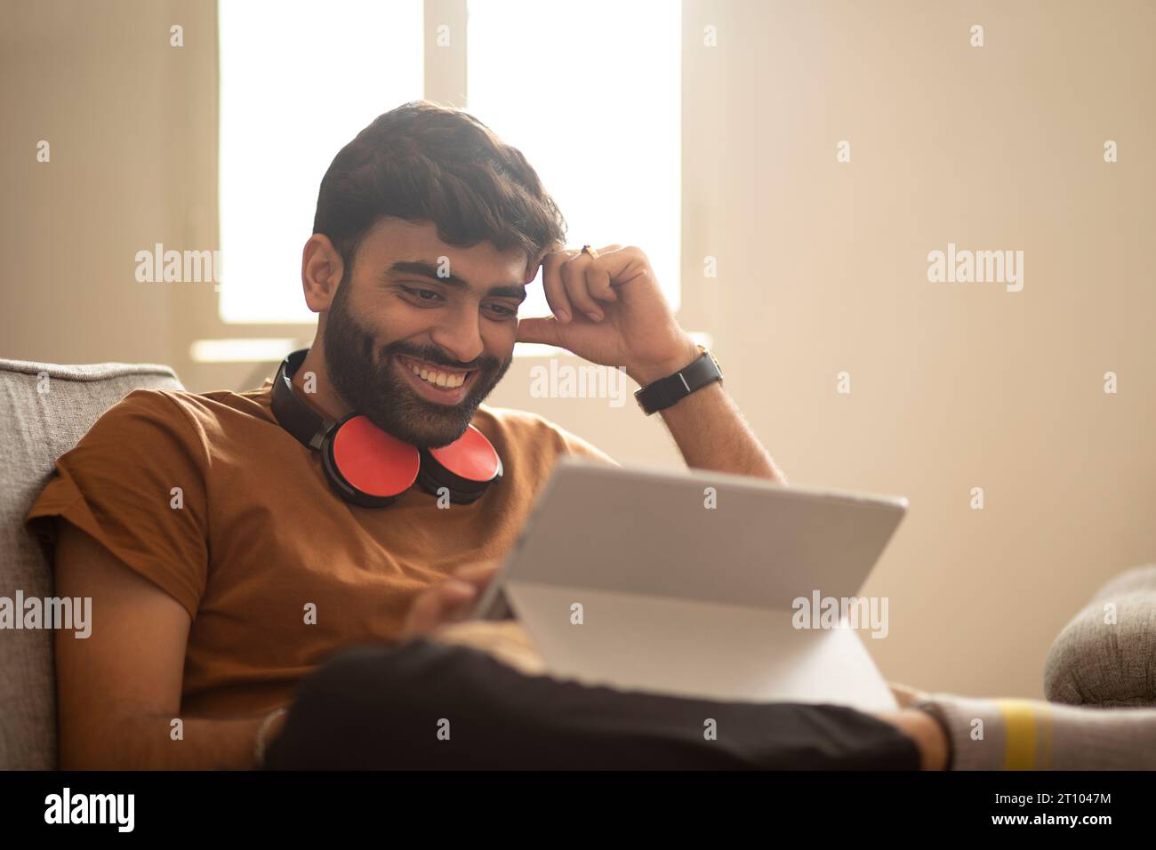 Un giovane che usa un tablet digitale mentre è seduto sul divano soggiorno Foto Stock
