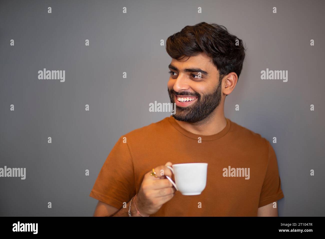 Ritratto di un uomo allegro che beve tè contro lo sfondo grigio Foto Stock