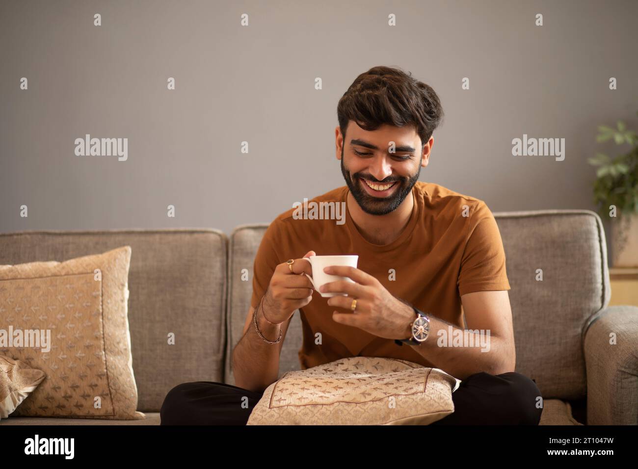 Un giovane beve tè mentre si rilassa sul divano nel soggiorno Foto Stock