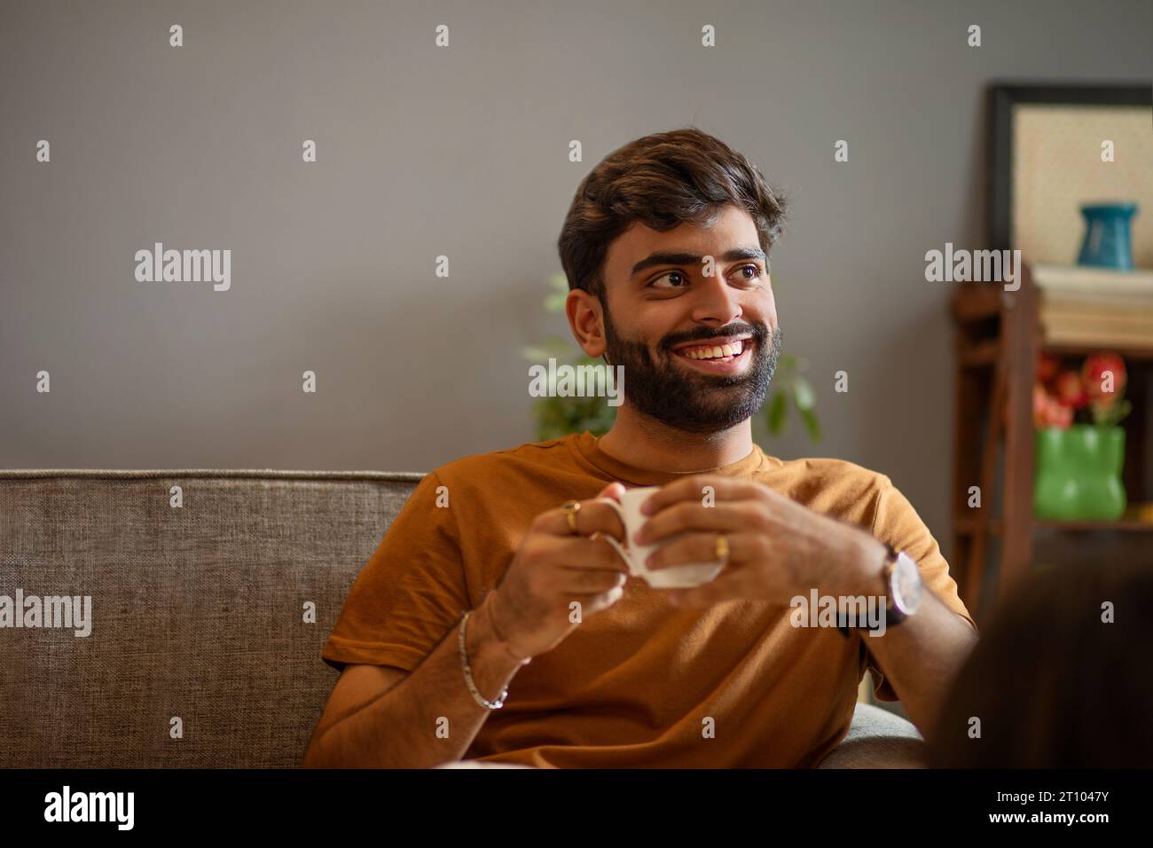 Un giovane beve tè mentre si rilassa sul divano nel soggiorno Foto Stock