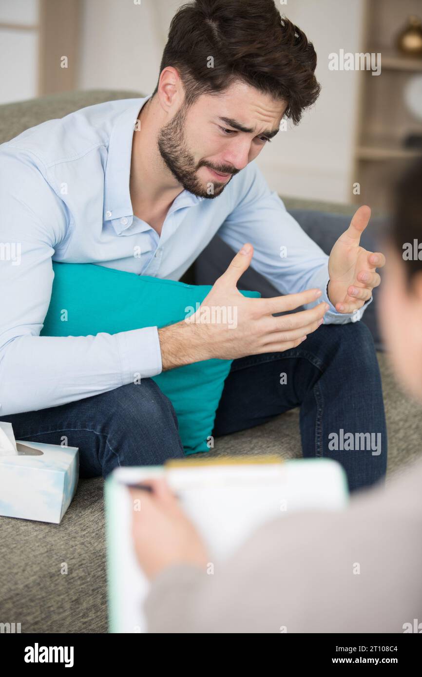 un uomo triste che parla con un terapista mentre lei ascolta Foto Stock