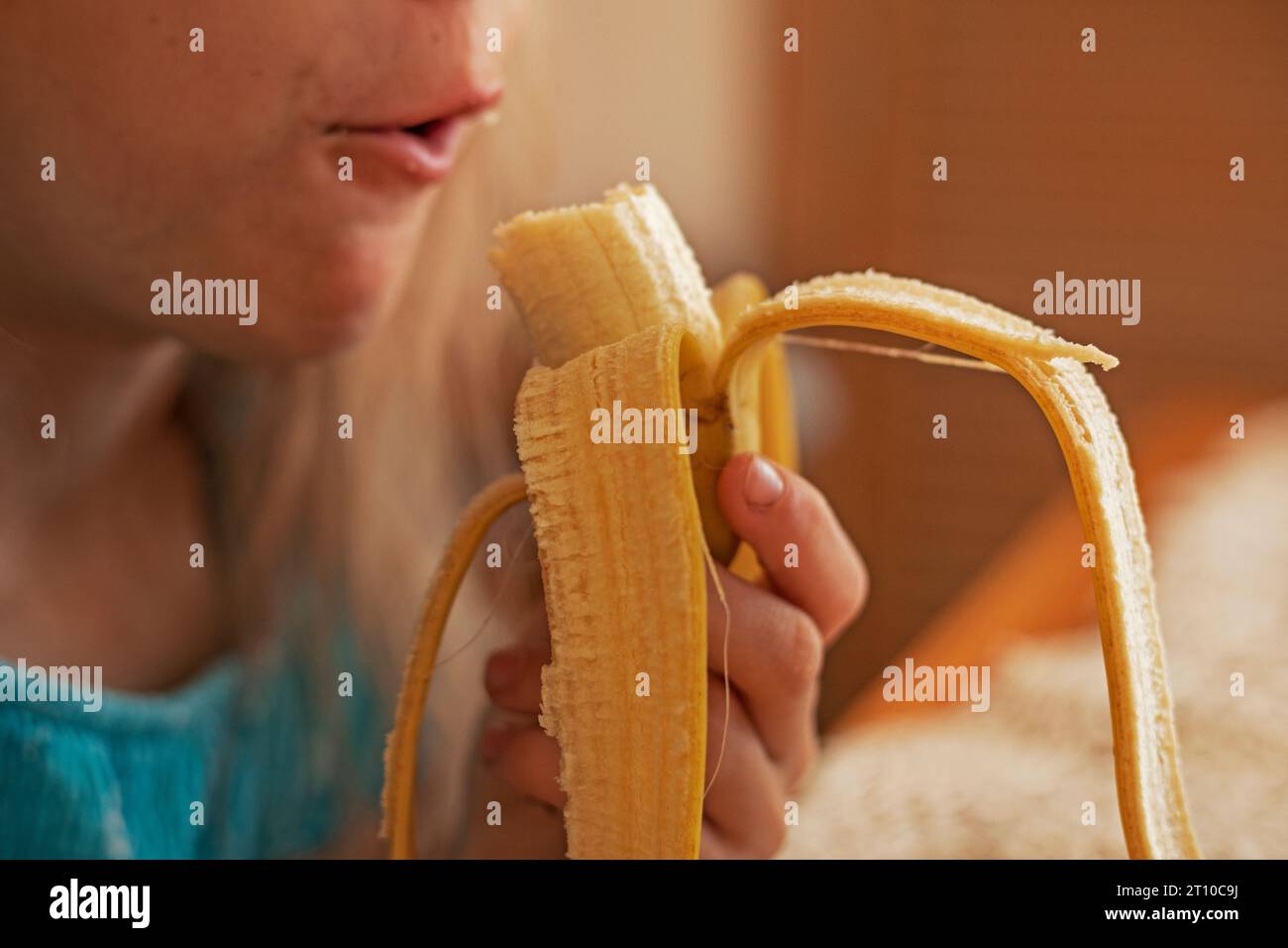 una ragazza dai lunghi capelli biondi mangia con piacere una dolce banana Foto Stock