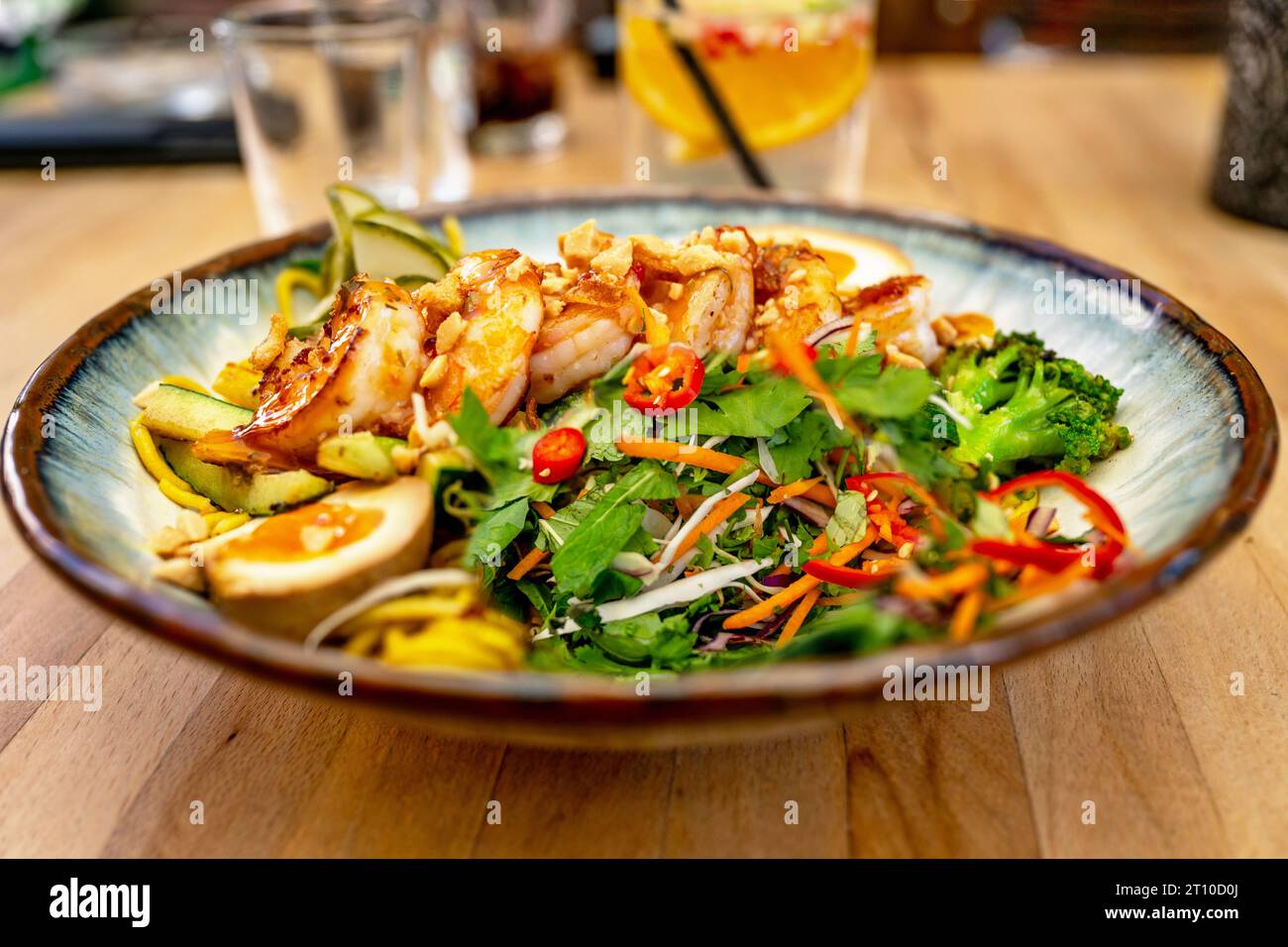 Insalata di erbe asiatiche agrodolci, uova sode e gamberi con peperoncino al piatto, drink in bicchiere, cena al tavolo del ristorante. Foto Stock